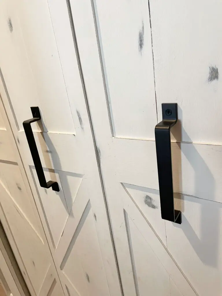 a close up of black barn door handles on a white barn door