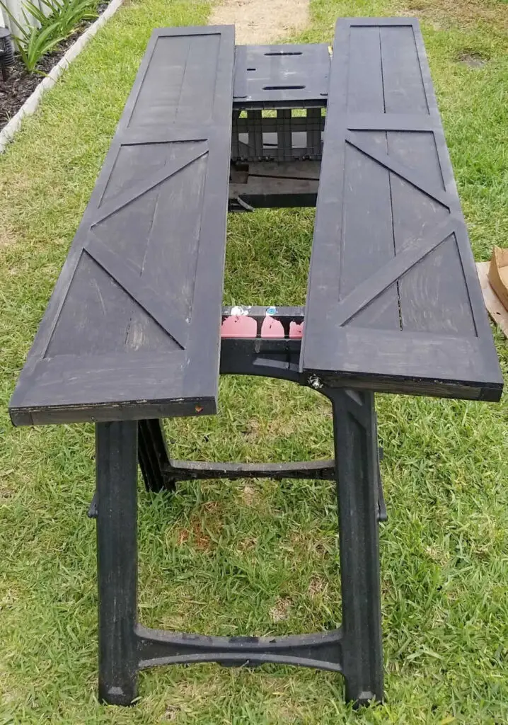 black stained bifold barn doors laid on stands on top of green grass