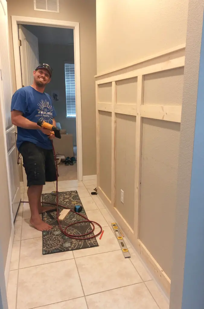 man standing with a nail gun about to nail in a board on a board and batten wall