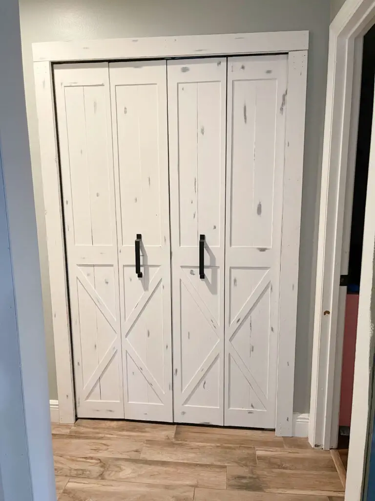 white bifold closet barn doors with white trim and black handles hung up in a hallway with grey walls