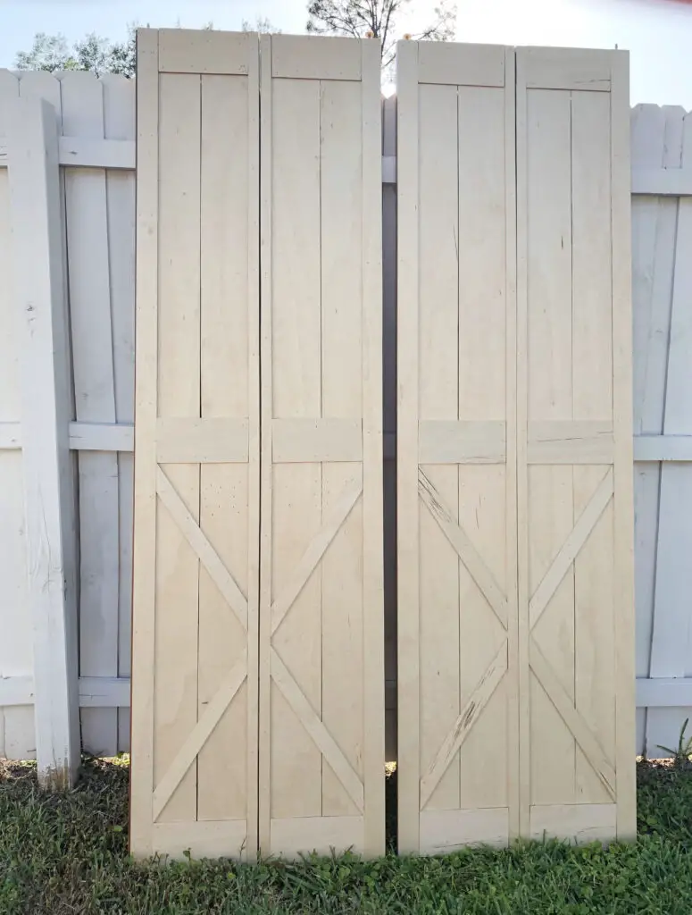 natural wood color bifold barn doors against a white fence outside