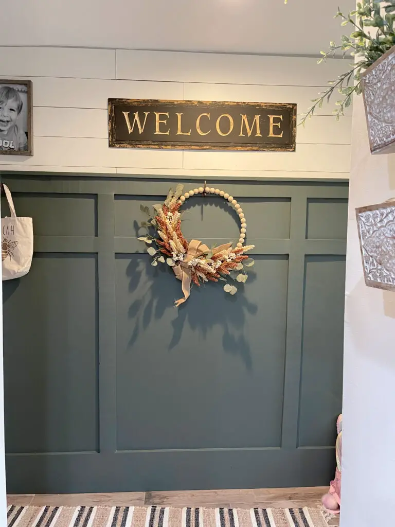 dark green board and batten wall with hooks and fall wreath and welcome sign