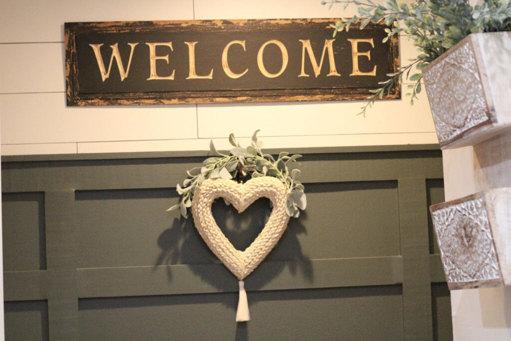 ivory heart wreath with greenery hanging in an entryway on a green board and batten wall