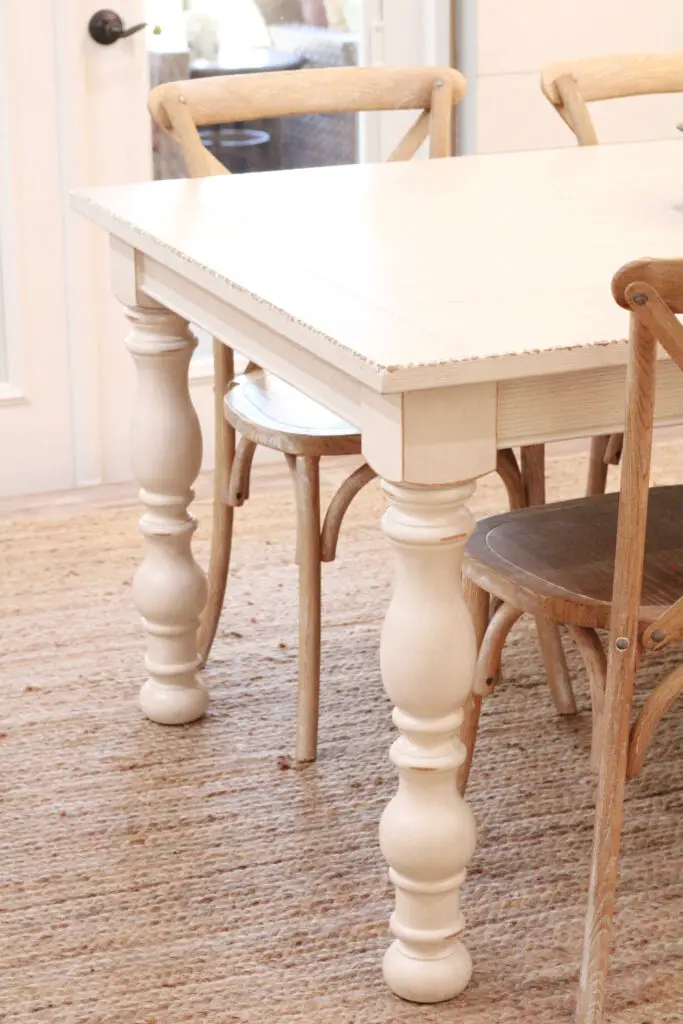 ivory dining table zoomed in on the table legs with cross back wood chairs and a jute rug