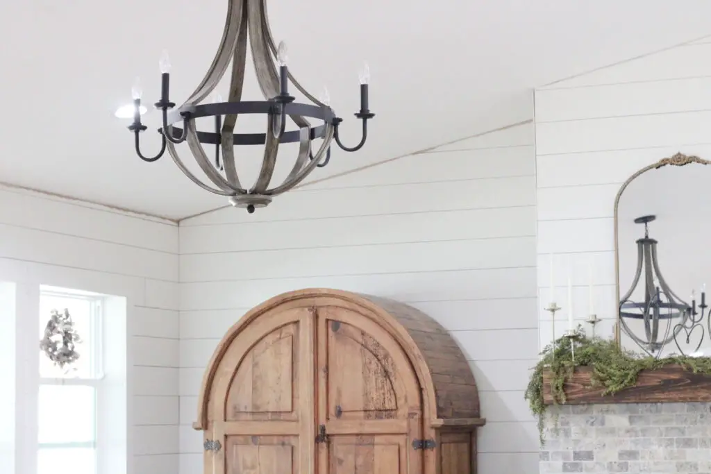 farmhouse wood and black metal dining room chandelier hanging with white shiplap walls and a wood armoire