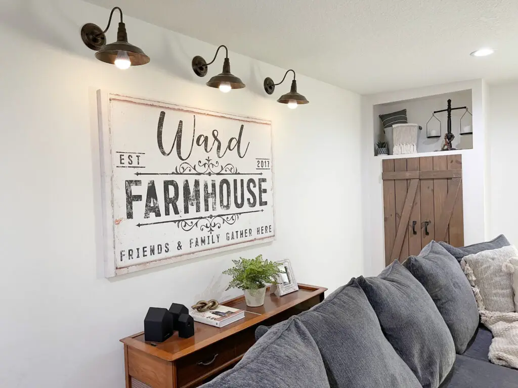 ward farmhouse large canvas sign with barn lights above it that are lit up behind a grey sectional