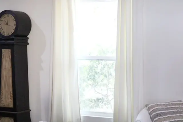 window with ivory curtains and black floor clock and white chair