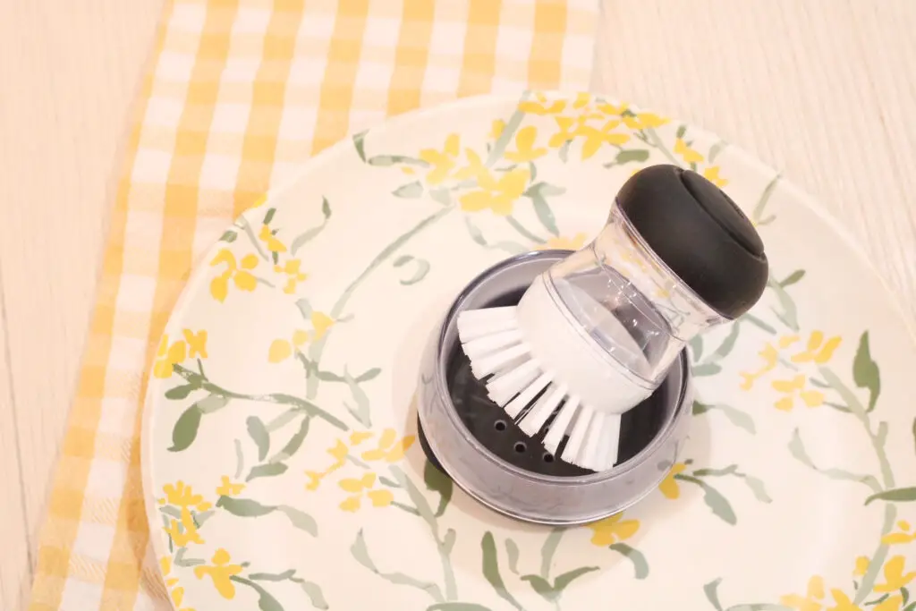 a kitchen dish brush that is black and white on a yellow flowered plate and a white and yellow dish cloth