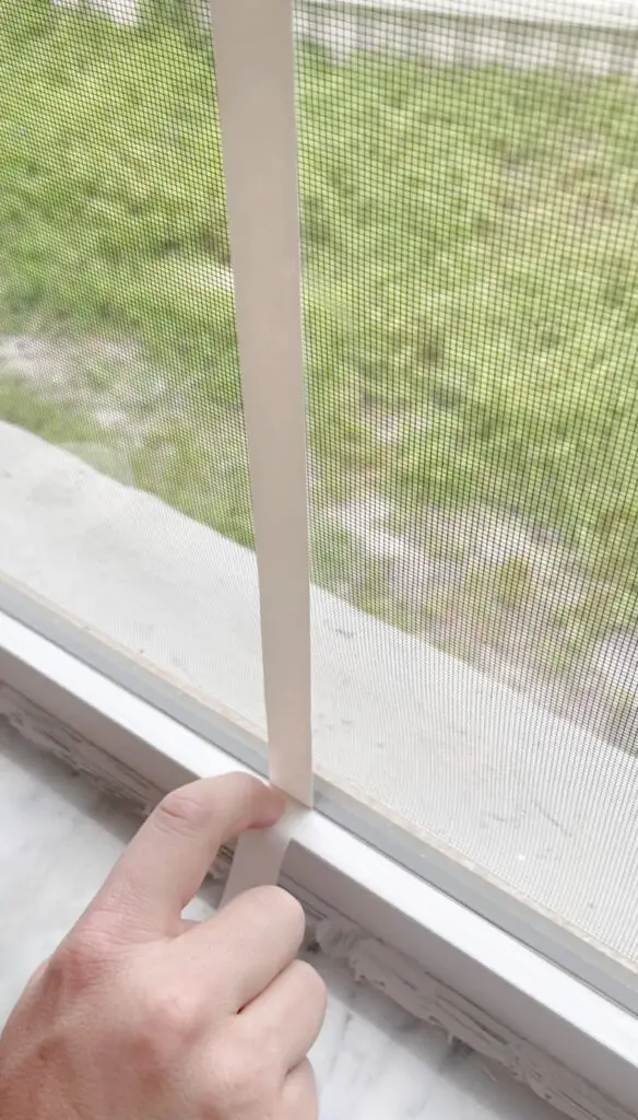 A hand pointing to a piece of white vinyl electrical tape on a window with white trim