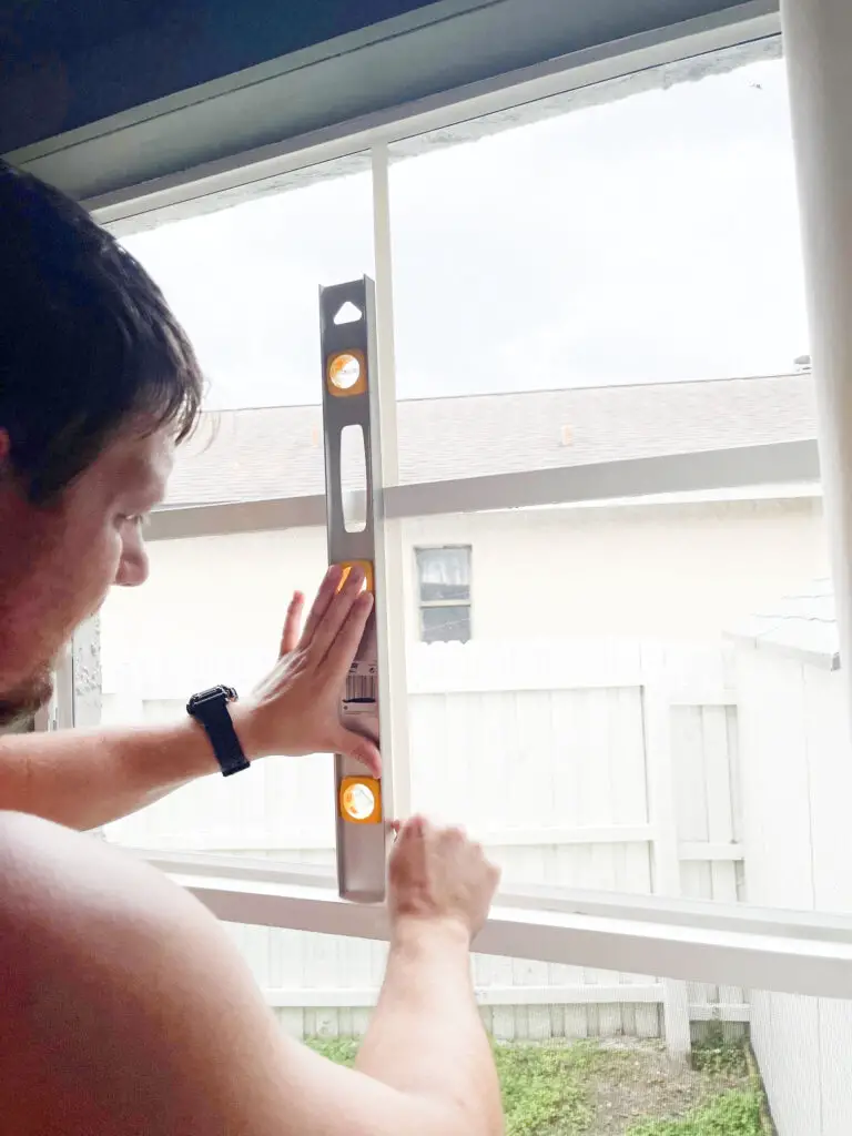 A man holding a level and white vinyl tape in front of a window