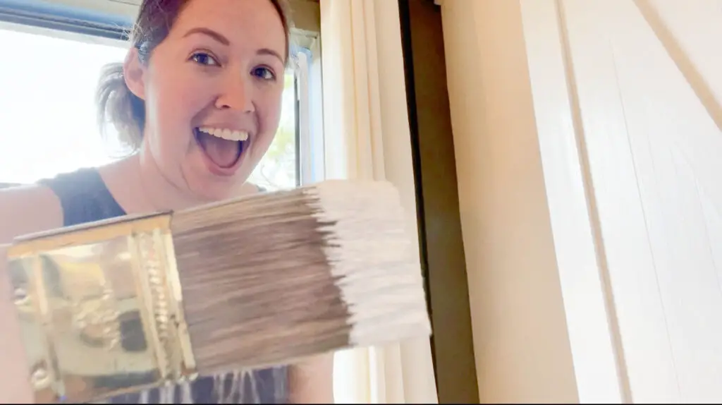 A woman holding a paint brush with white paint on it standing in front of a window