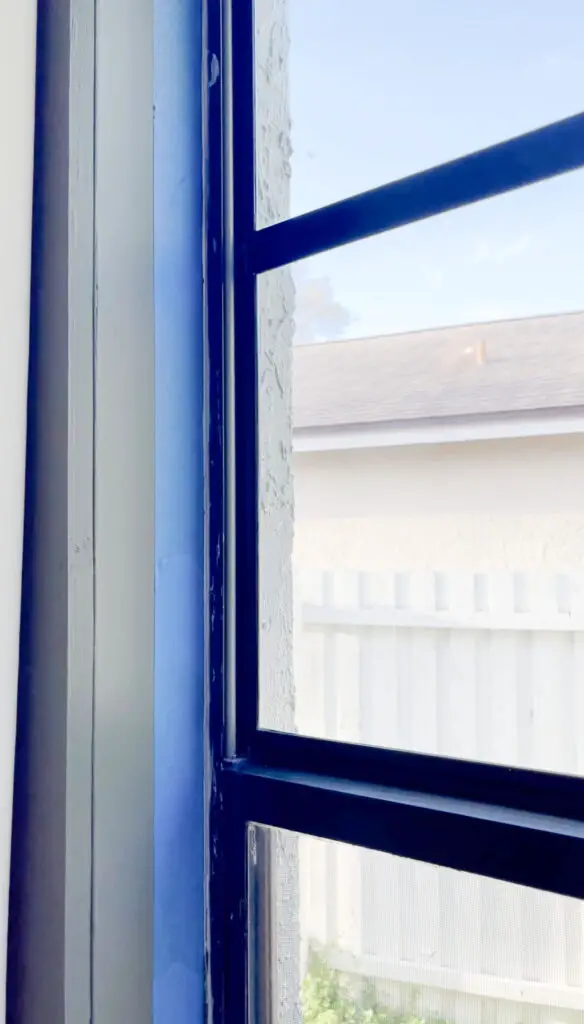 Blue painters tape around a window with black trim and a green wall