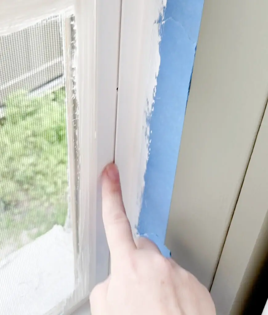 A hand pointing to the creases in a window where the window opens on a white painted window