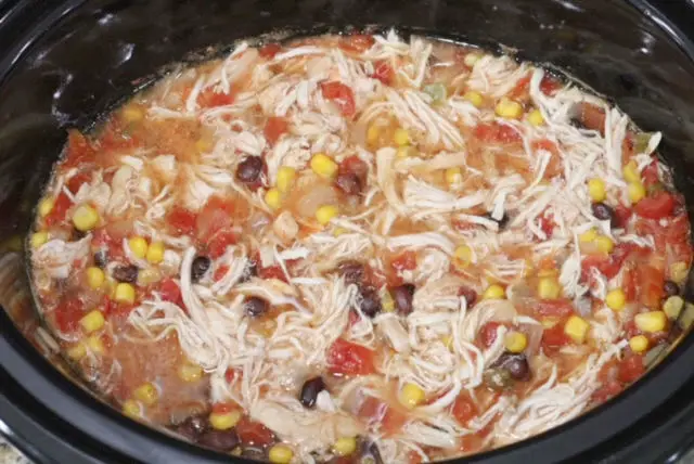a close up of a black crockpot with shredded chicken, black beans, corn, onion in it