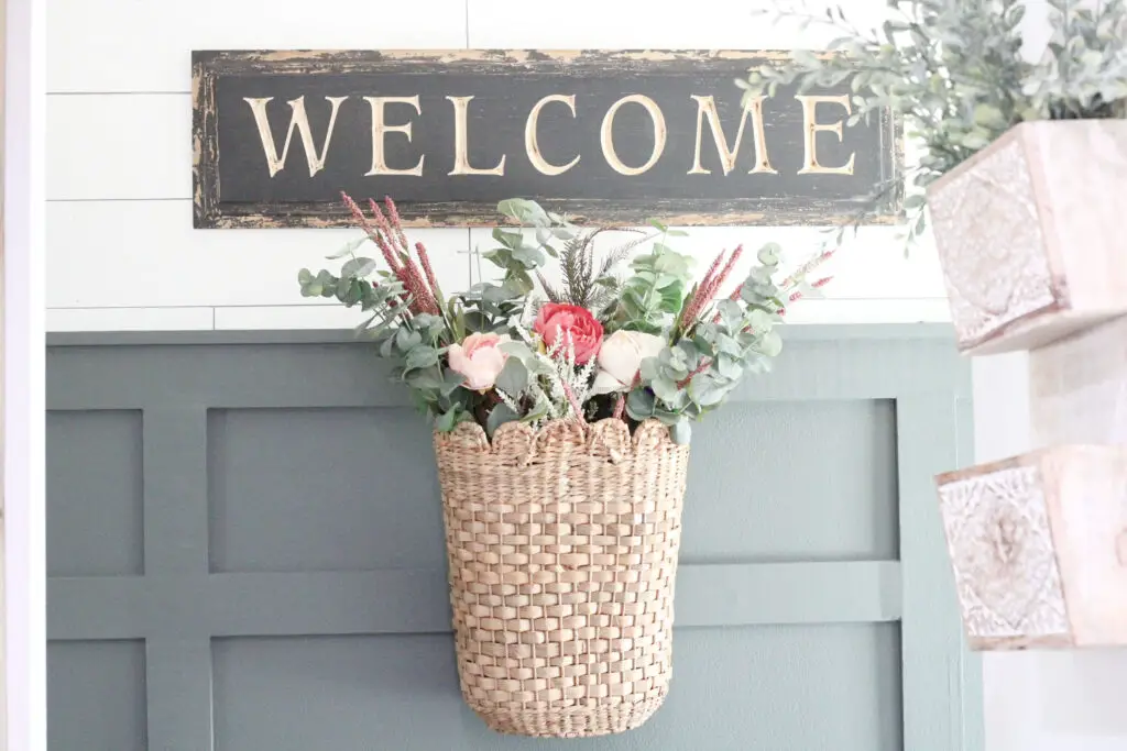 basket with pink peonies and greenery hanging in a farmhouse entryway against a green board and batten wall, and white shiplap wall