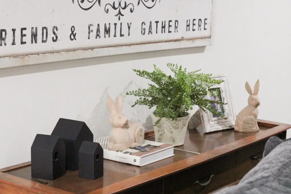 a wooden console table with 3 little black houses, 2 wooden bunnies, some greenery and a book for spring decor