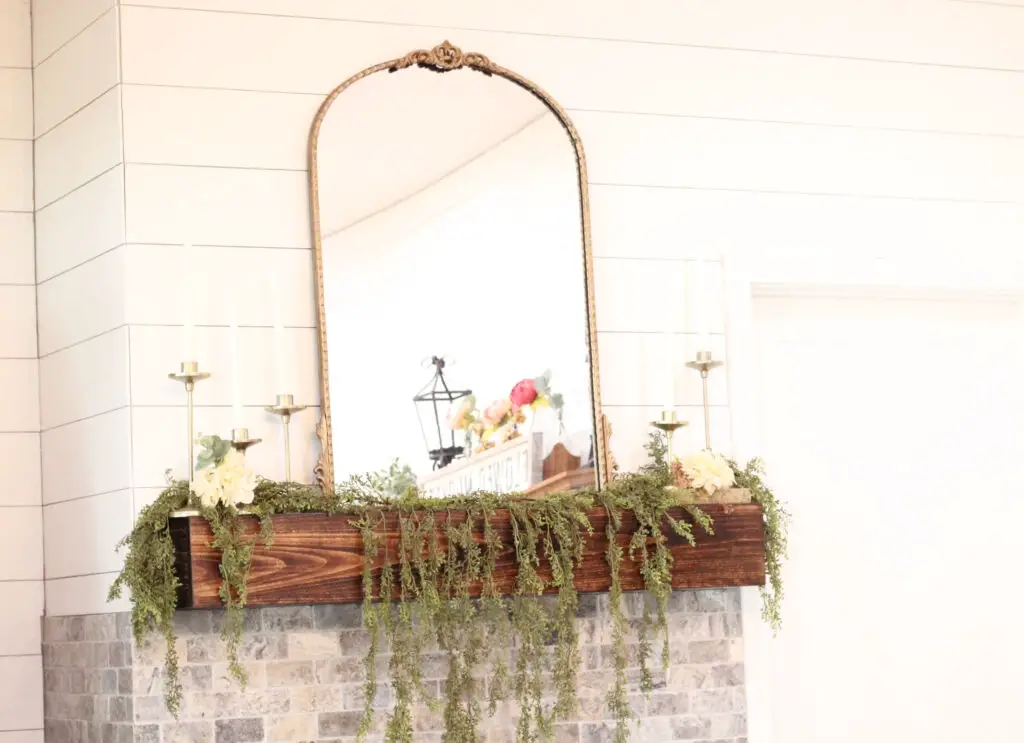a wood mantel with gold mirror and greenery and white florals for spring
