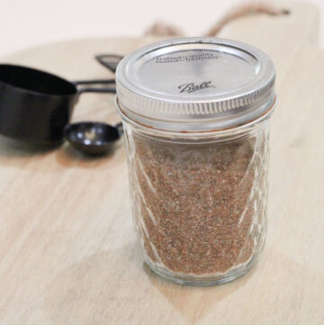 Close up of a glass mason jar with taco seasoning in it and black measuring spoons behind it