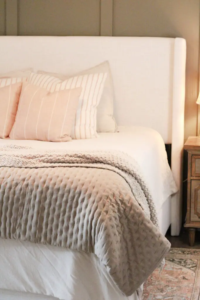 Green board and batten wall with a white linen king bed on it with wood nightstands and orange and green patterned rug on the floor under the bed in a master bedroom 