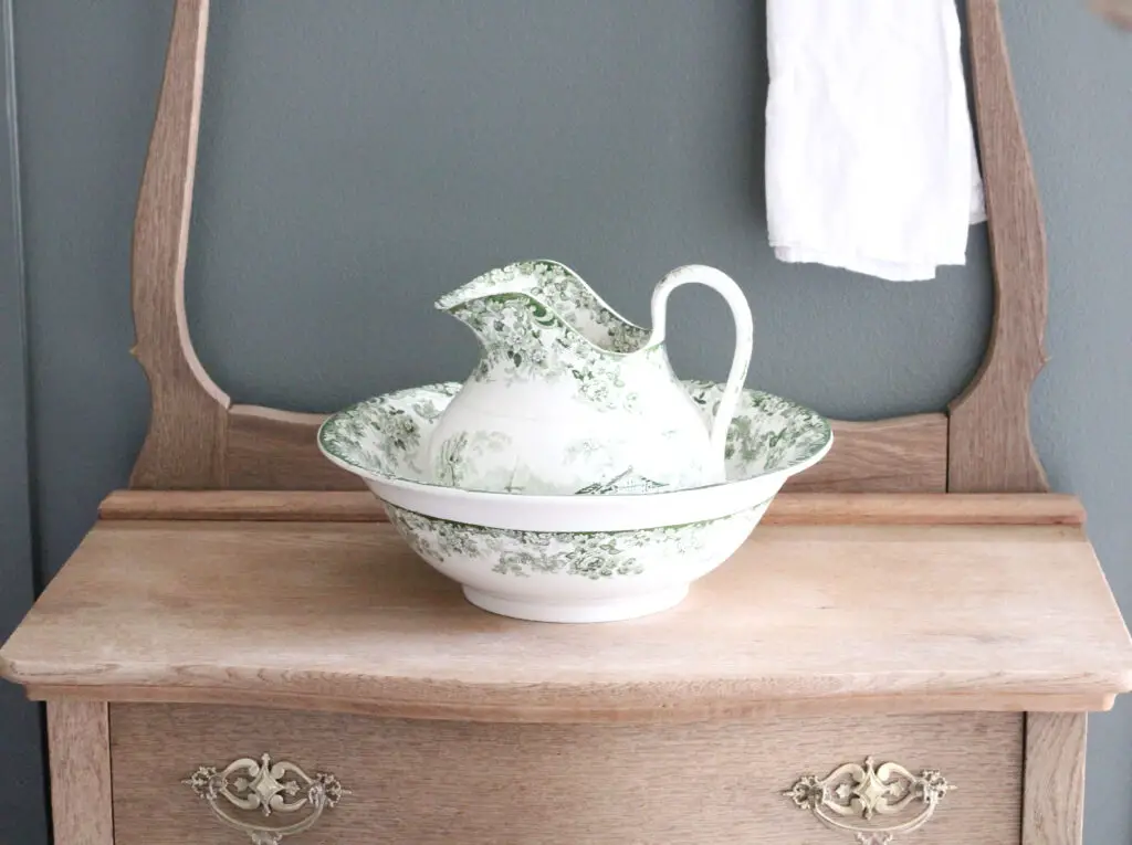 Wood washstand with white and green bowl and pitcher on top of it with a white towel hanging