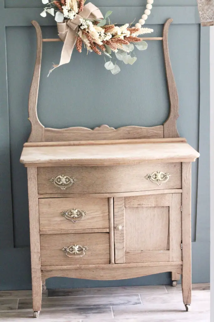 natural, light wood washstand against a dark green wall with gold brass knobs