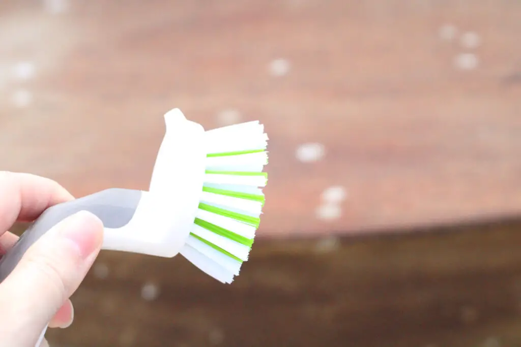 a close up of a white dish brush and in the background is a wood washstand to scrub 