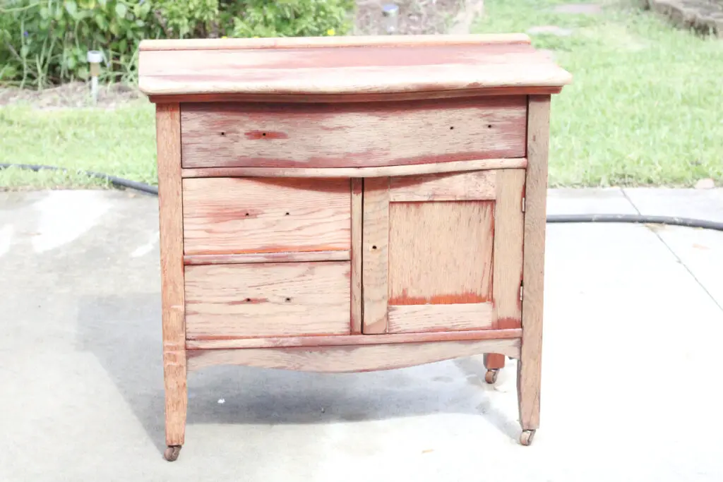 wood washstand in the sun with parts stain and parts natural wood showing as it is drying
