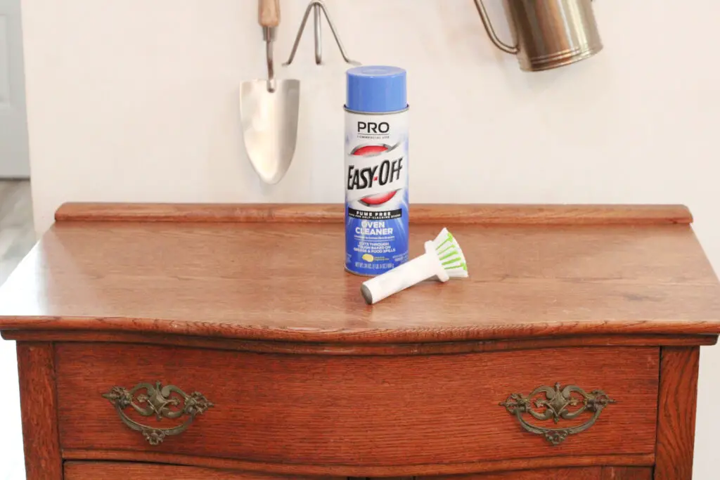 Wood washstand dresser with easy off oven cleaner spray can on top and a white dish brush