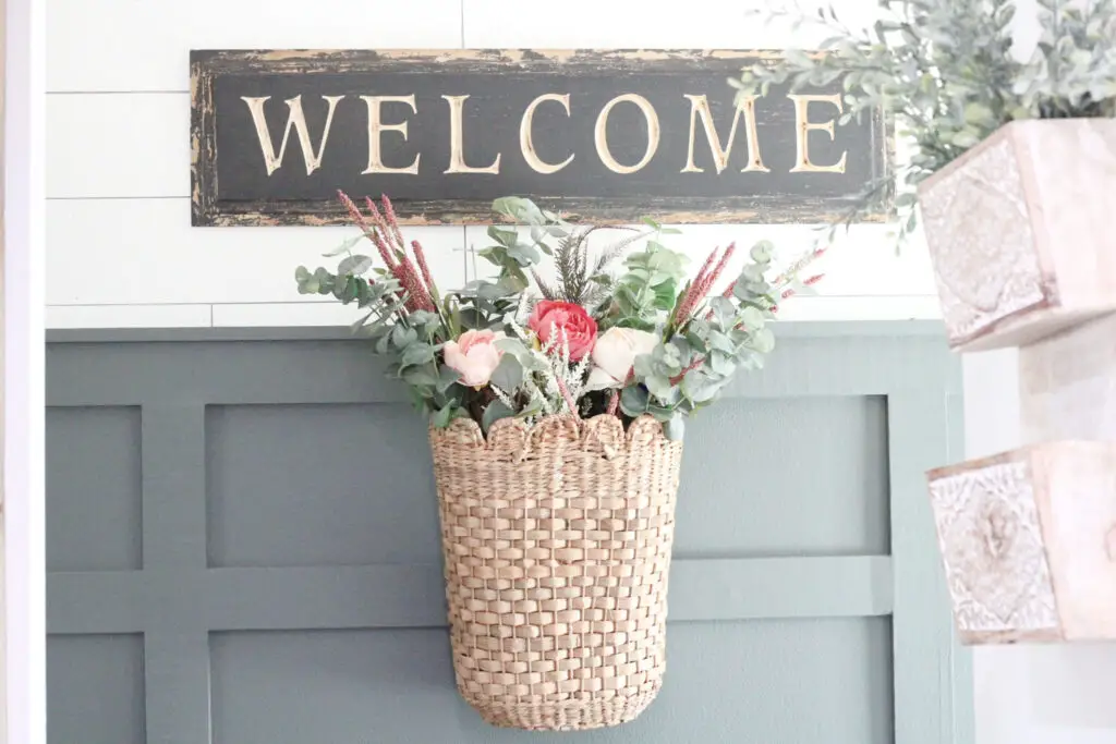 Close up of a basket with pink and green spring florals hanging on a dark green board and batten wall