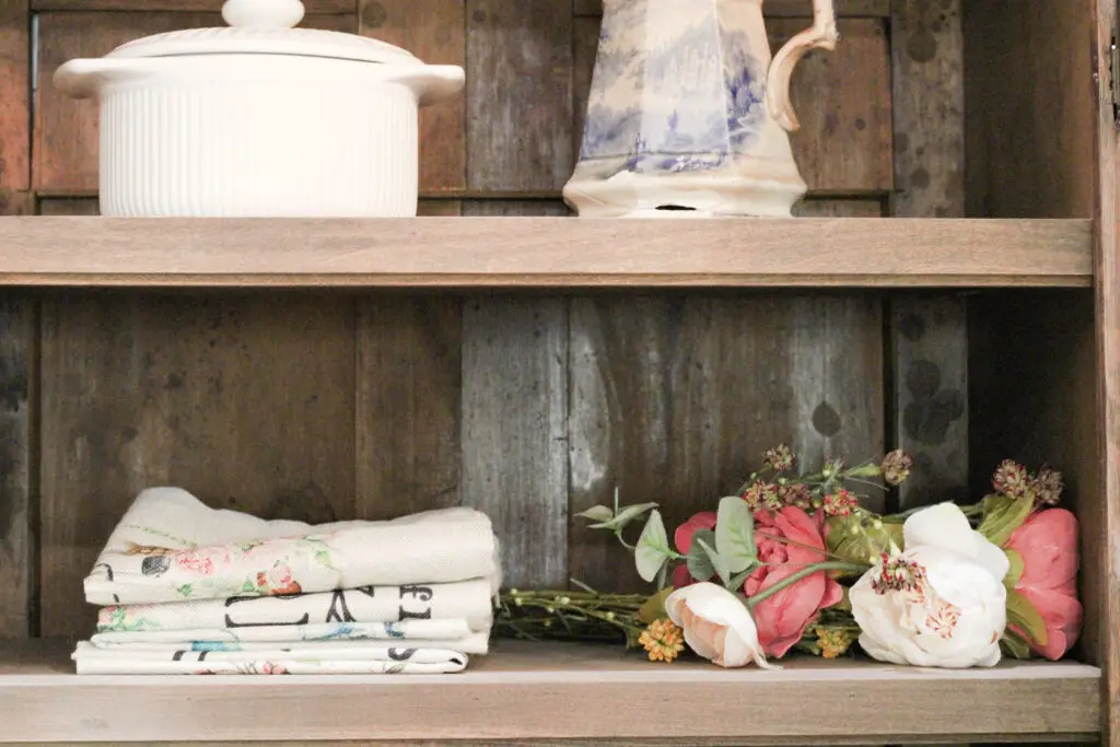 close up of wood colored shelves with folded up linen pillow covers with pink spring florals beside it. 