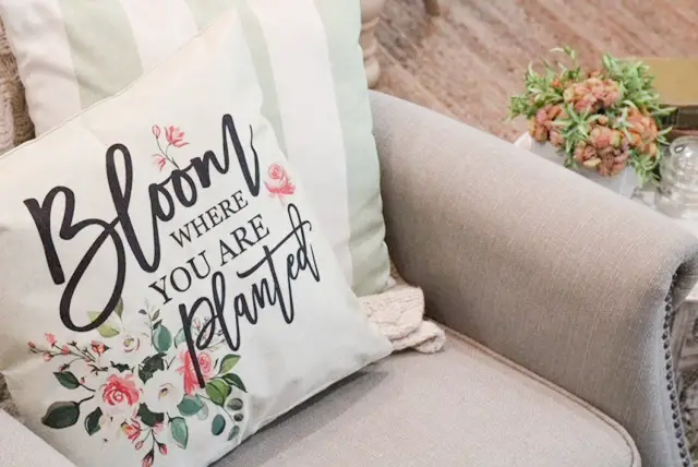 Close up of a linen pillow cover with spring pink and green florals on it on a gray chair. 