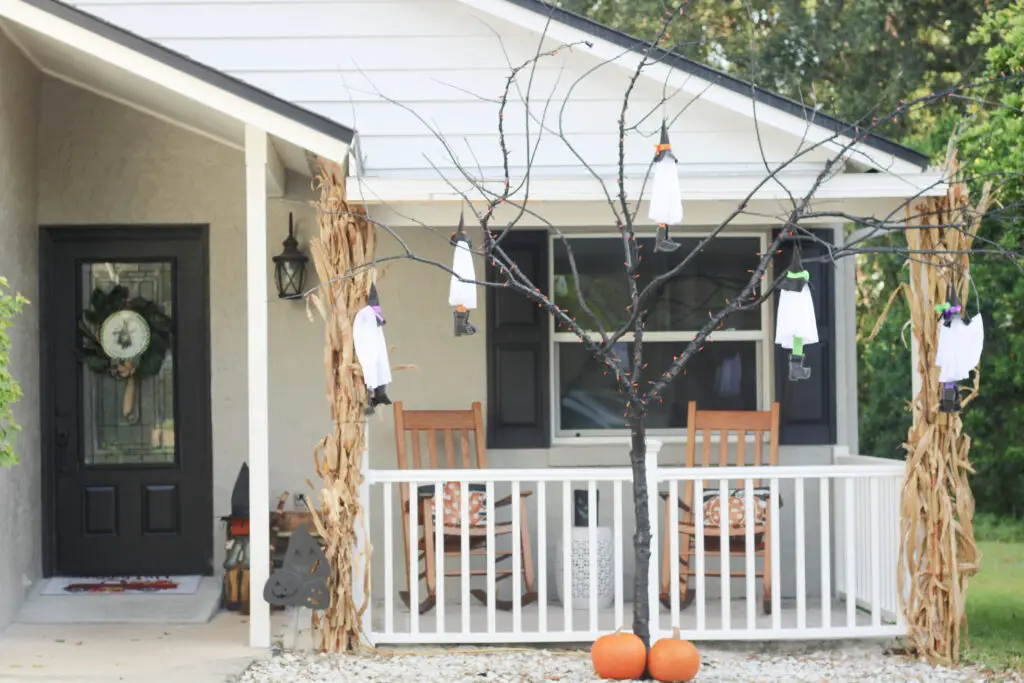 outside of the front of a white and grey house with a black tree in front of it with no leave and white ghosts hanging off of it and 2 orange pumpkins at the bottom of the tree. 
