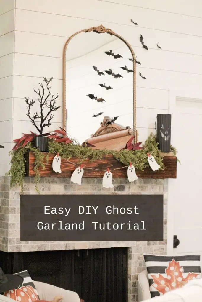 A Halloween decorated fireplace wood mantel with a white paper book ghost garland on a burlap string hanging with orange clothes pins, with a black jack o lantern and a black tree on the mantel. With the text in a black background and white text that says: "Easy DIY Ghost Garland Tutorial"