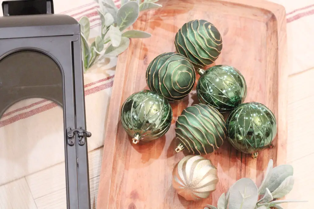 close up of green and gold Christmas ornaments on a wood tray with greenery stems and a black lantern