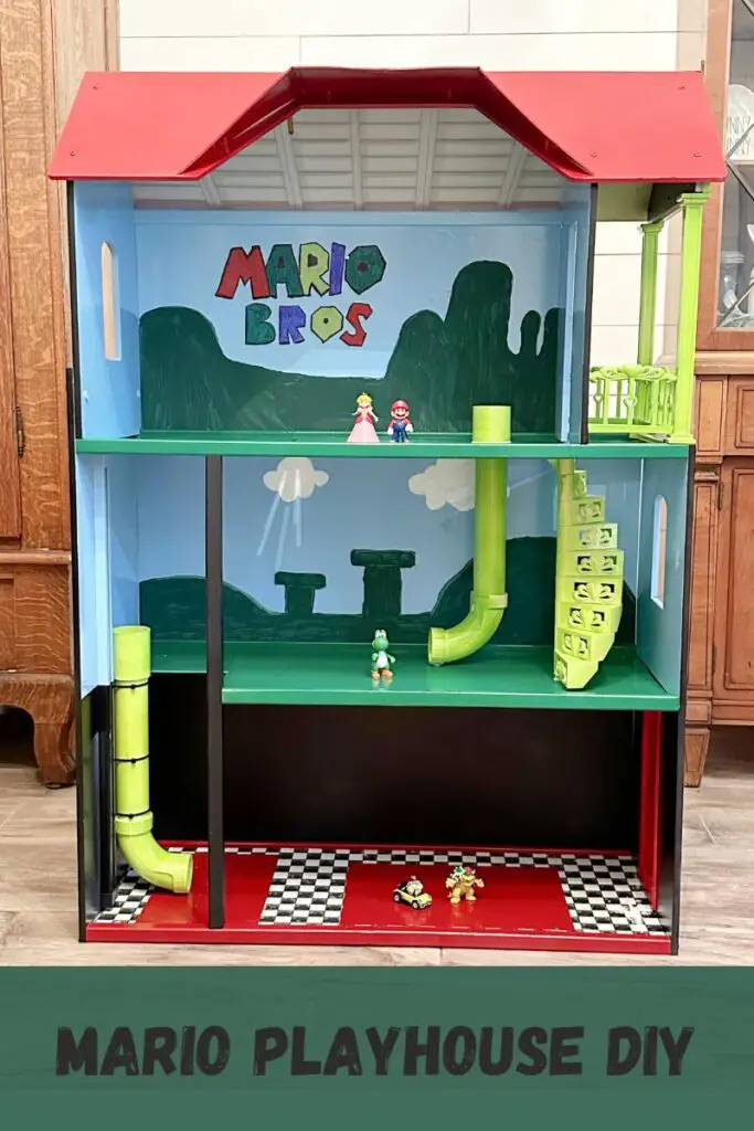 Close up of a Mario playhouse with red roof and Mario Bros painted on the back wall, with green hills, green tunnels, and plastic Mario characters inside the house. 