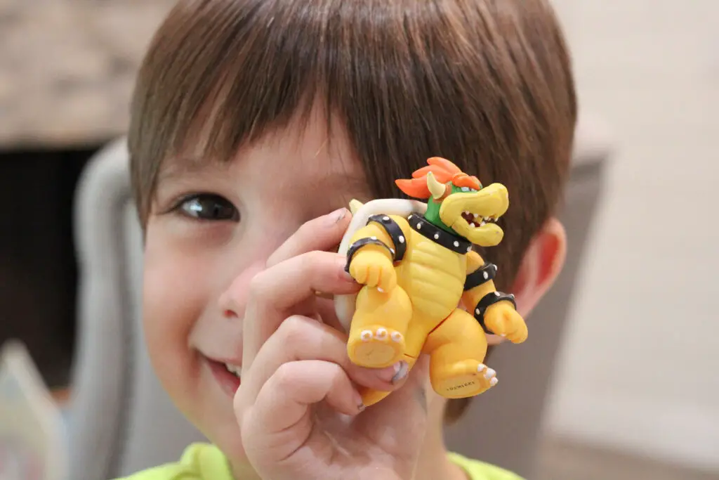 close up of a little boy with brown hair holding up a green and yellow Bowser character from Mario