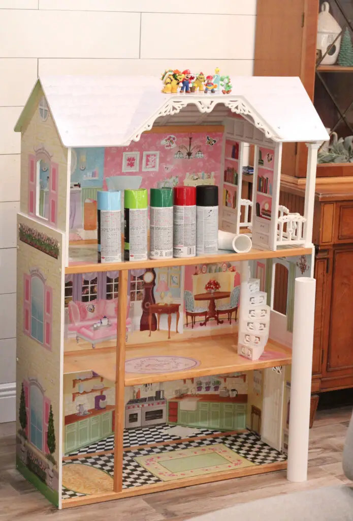 close up of a wooden dollhouse with green, red, blue, and black spray paint cans on it. 