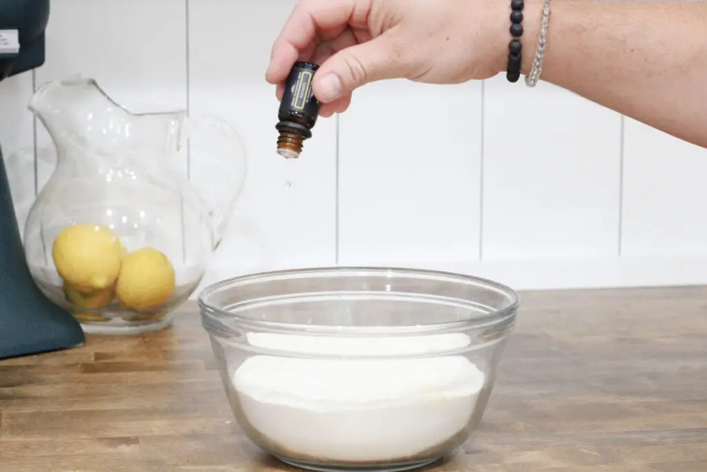 Close up of a man holding essential oils and a drop coming out into a glass bowl with white powder in it.