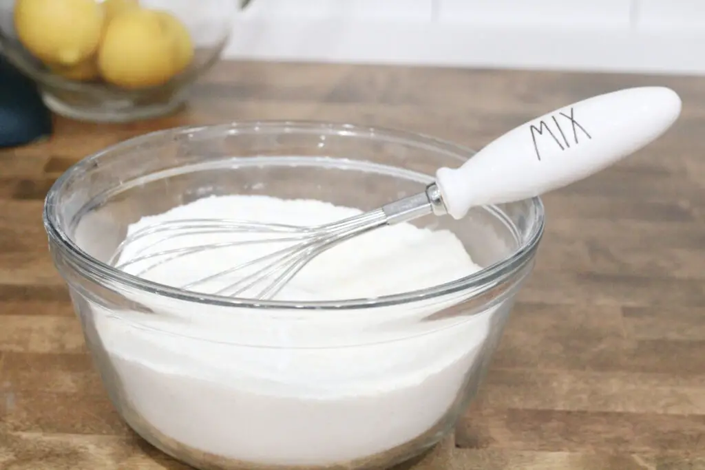 close up of a glass bowl with white powder and a metal and white whisk that says mix on it. 