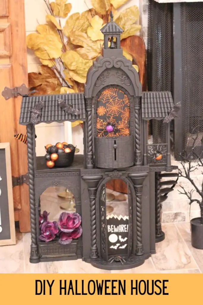 Close up of a black Halloween house with orange spider webs, purple and black spiders, purple flowers, the words "DIY Halloween House" written at the bottom