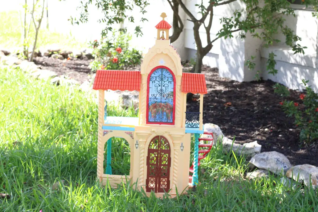 a dollhouse that is yellow, red, brown, and blue outside on green grass