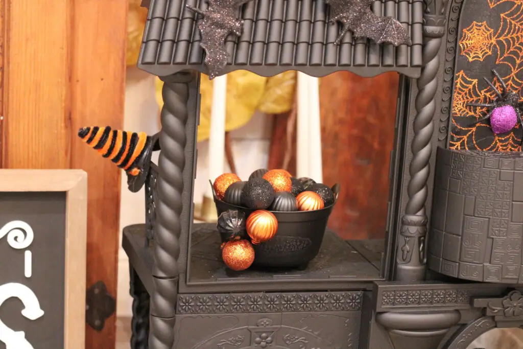 Close up of a mini black witches cauldron with black and orange ornaments coming out of it and a black and orange mini witches hat. 