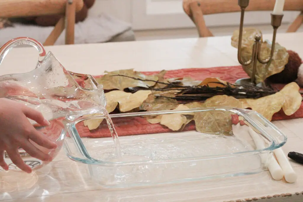 Close up of water bring poured out of a glass pitcher into a glass baking container. 