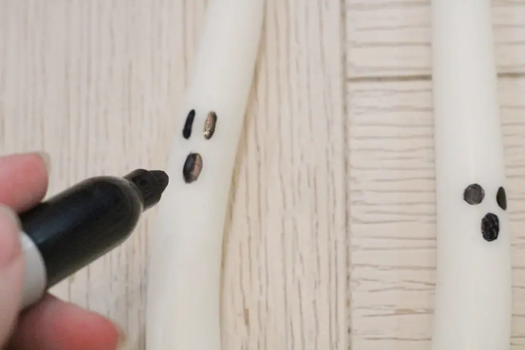 Close up of a white candlestick with a black sharpie drawing a ghost face onto it. 