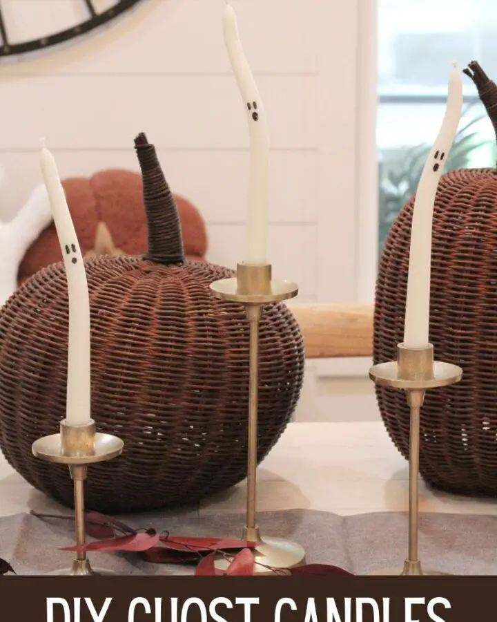 3 white tapered candles with black ghosts faces on them in gold candlestick holders, with brown wicker pumpkins behind them, on a white dining table with the text "DIY Ghost Candles" written at the bottom