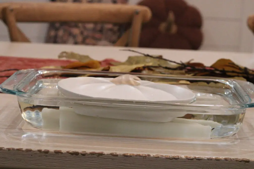 close up of a white pumpkin plate onto of white candlesticks in a glass baking dish in water. 