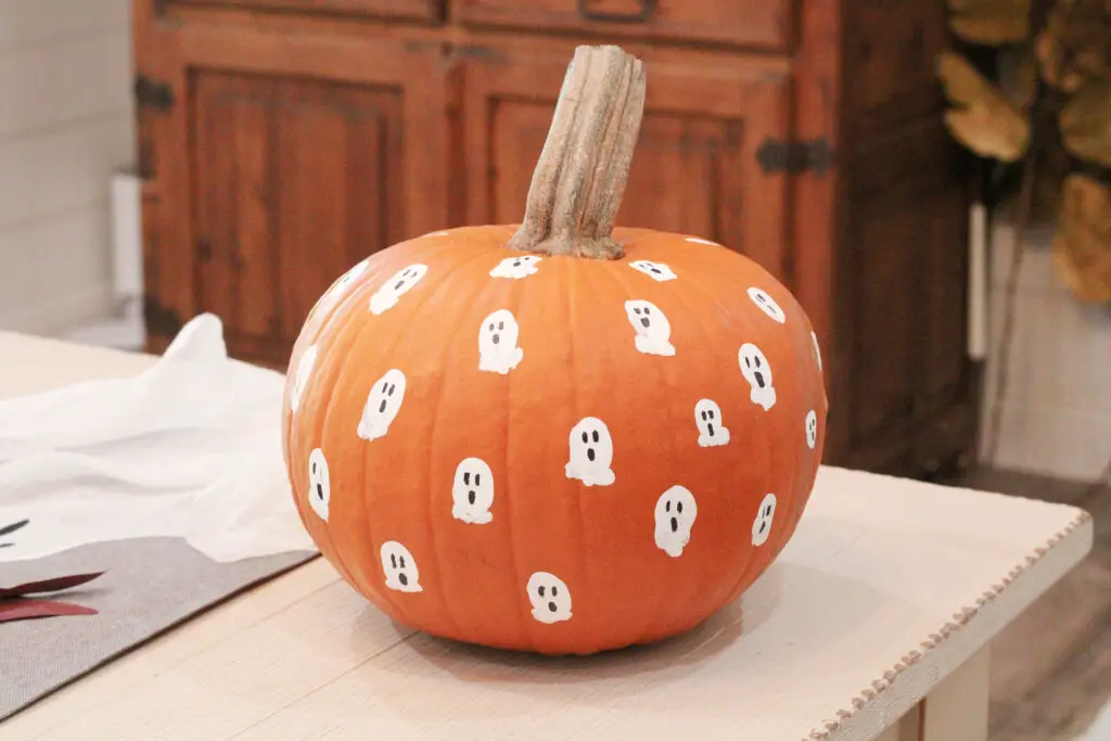 Close up of a real orange pumpkin with white thumbprints all over it and black ghost faces on a white dining table
