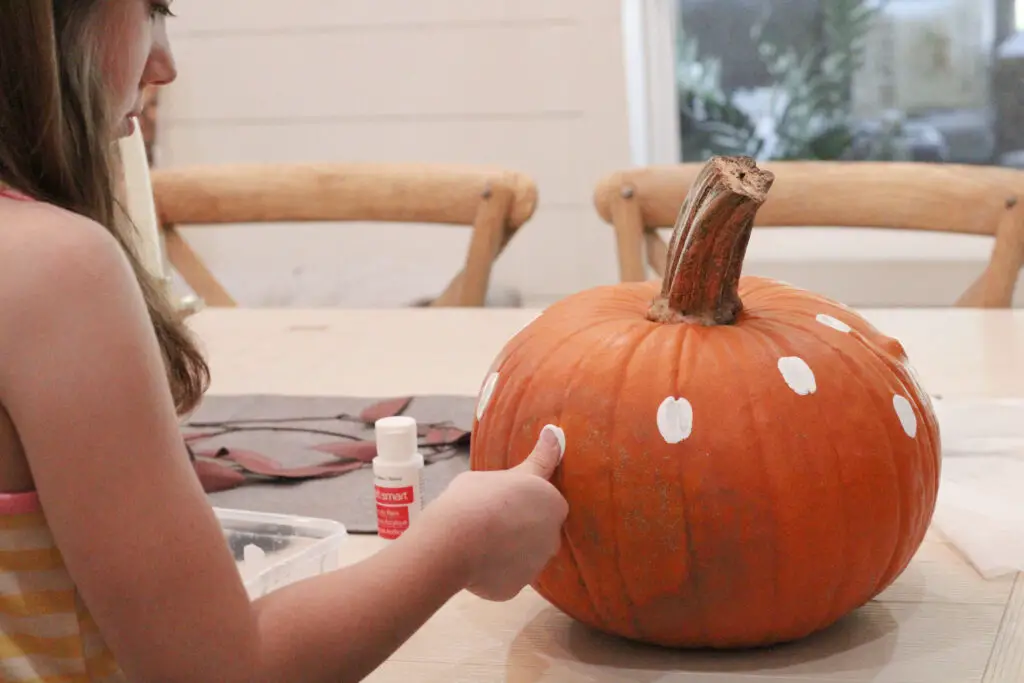 Close up of a real orange pumpkin with a little girl putting her thumbprint in white paint and onto the pumpkin. 