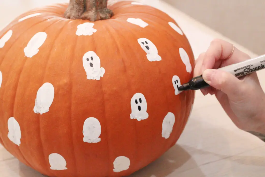 Close up of a real orange pumpkin, with a hand drawing ghost faces onto the white paint with a black marker