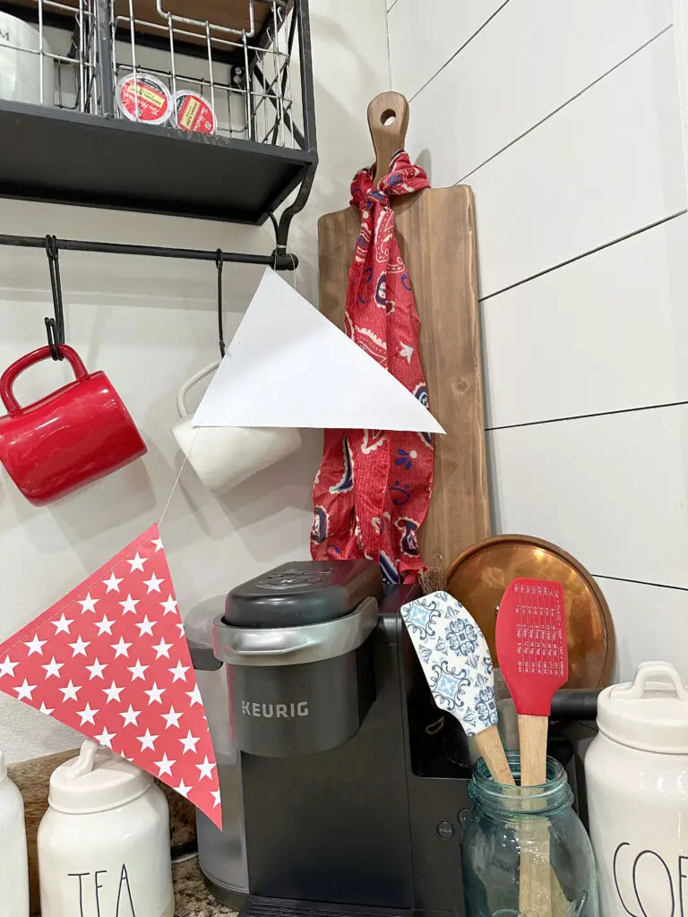 Close up of a red mug, white mug, coffee pods, kerig machine, cutting board, with red, white, and blue scarf hanging from it.